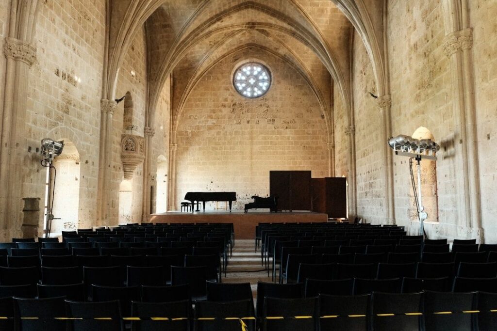 Salle de concert vide avec piano à queue et rangées de chaises noires